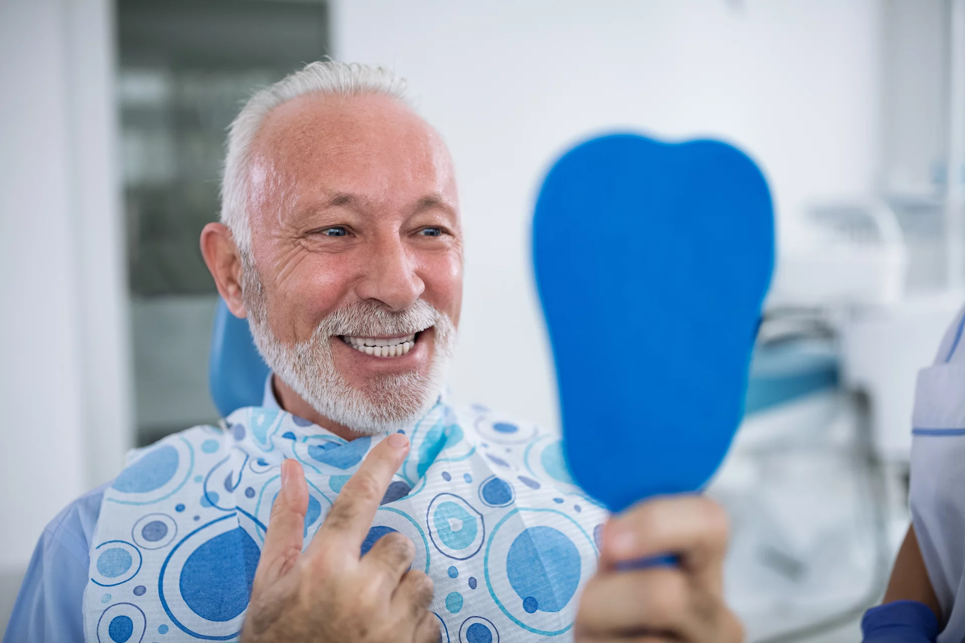 Smiling and satisfied patient after treatment looks at teeth in mirror
