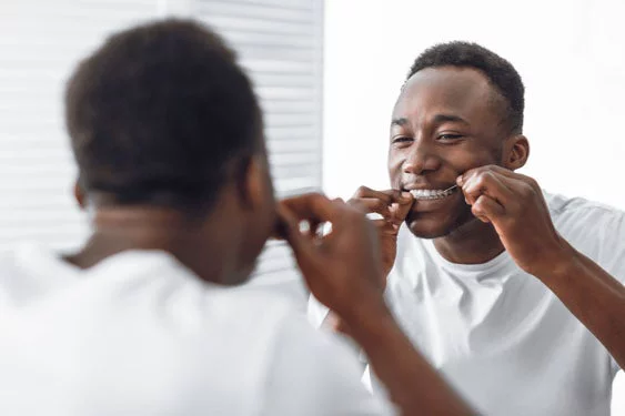 African man flossing his teeth in front of the mirror