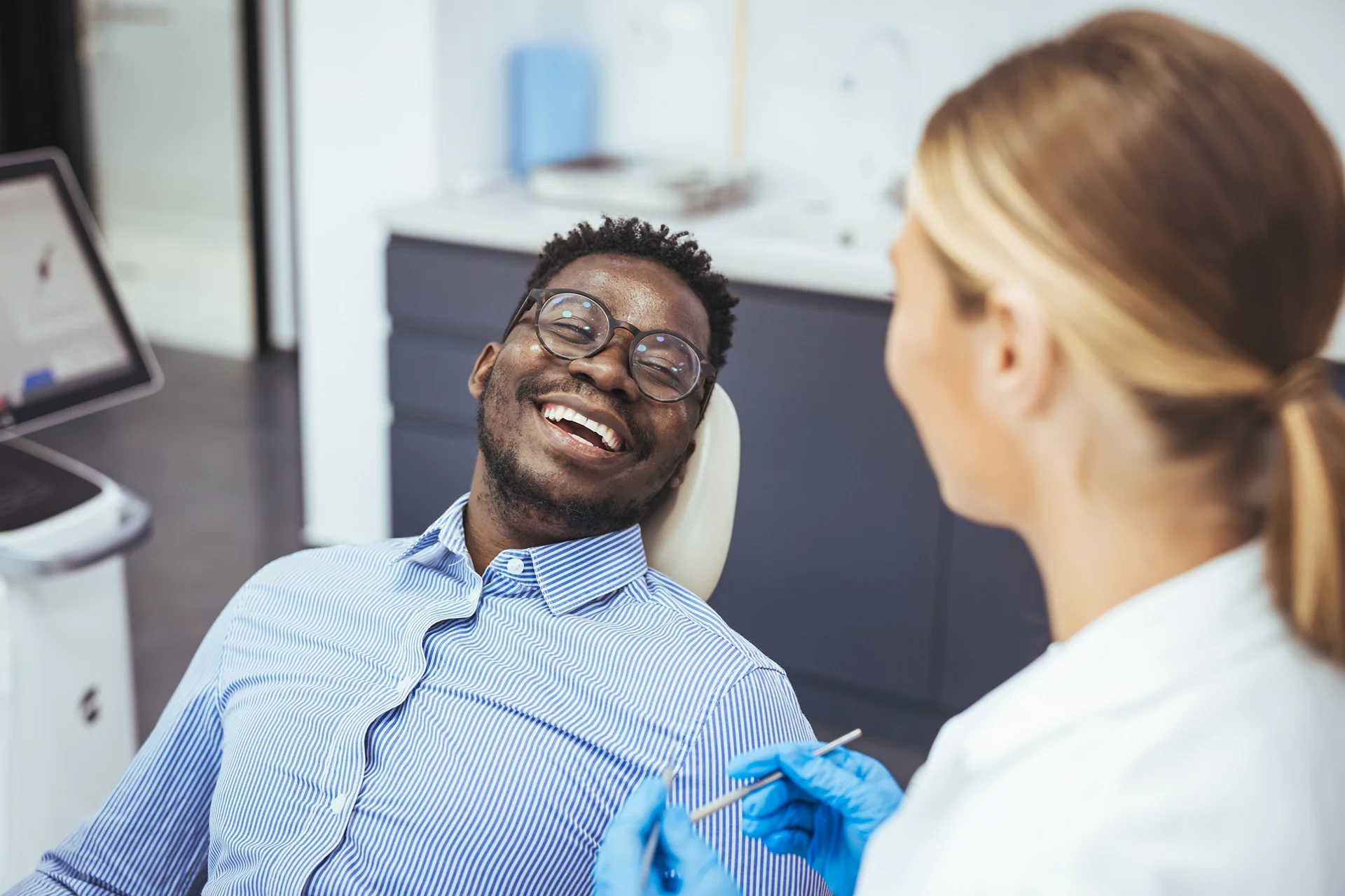 Smiling african guy in dentist chair looking with trust at his doctor, close up. Young African American Man Getting Teeth Treatment With Professional Stomatologist At Modern Clinic
