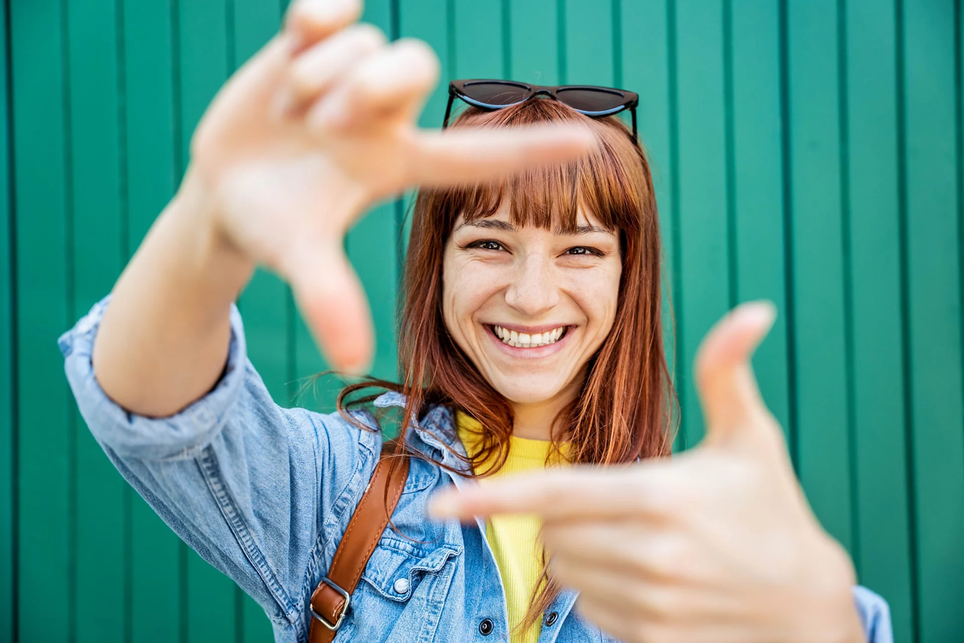 Young pretty woman making frame shape with hands on a green background - Happy tourist girl smiling at camera - Focus on face
