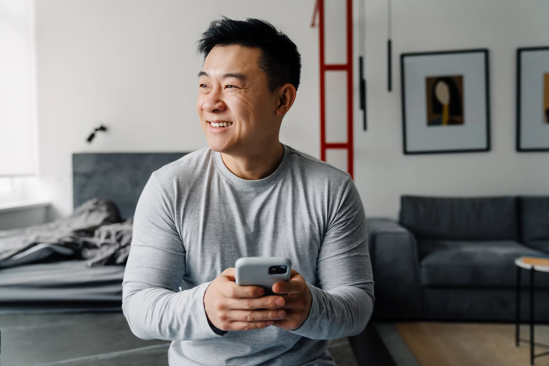 Brunette adult asian man smiling and using cellphone at home