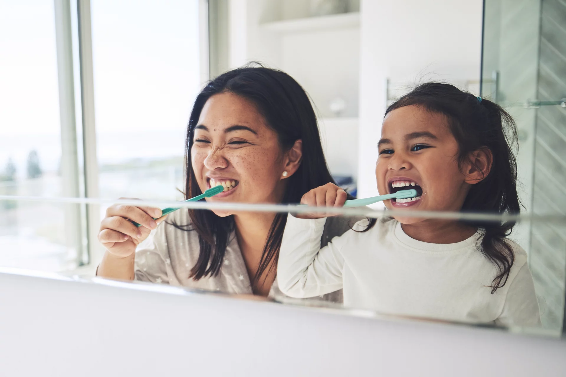 Mother and daughter brushing their teeth, smiling