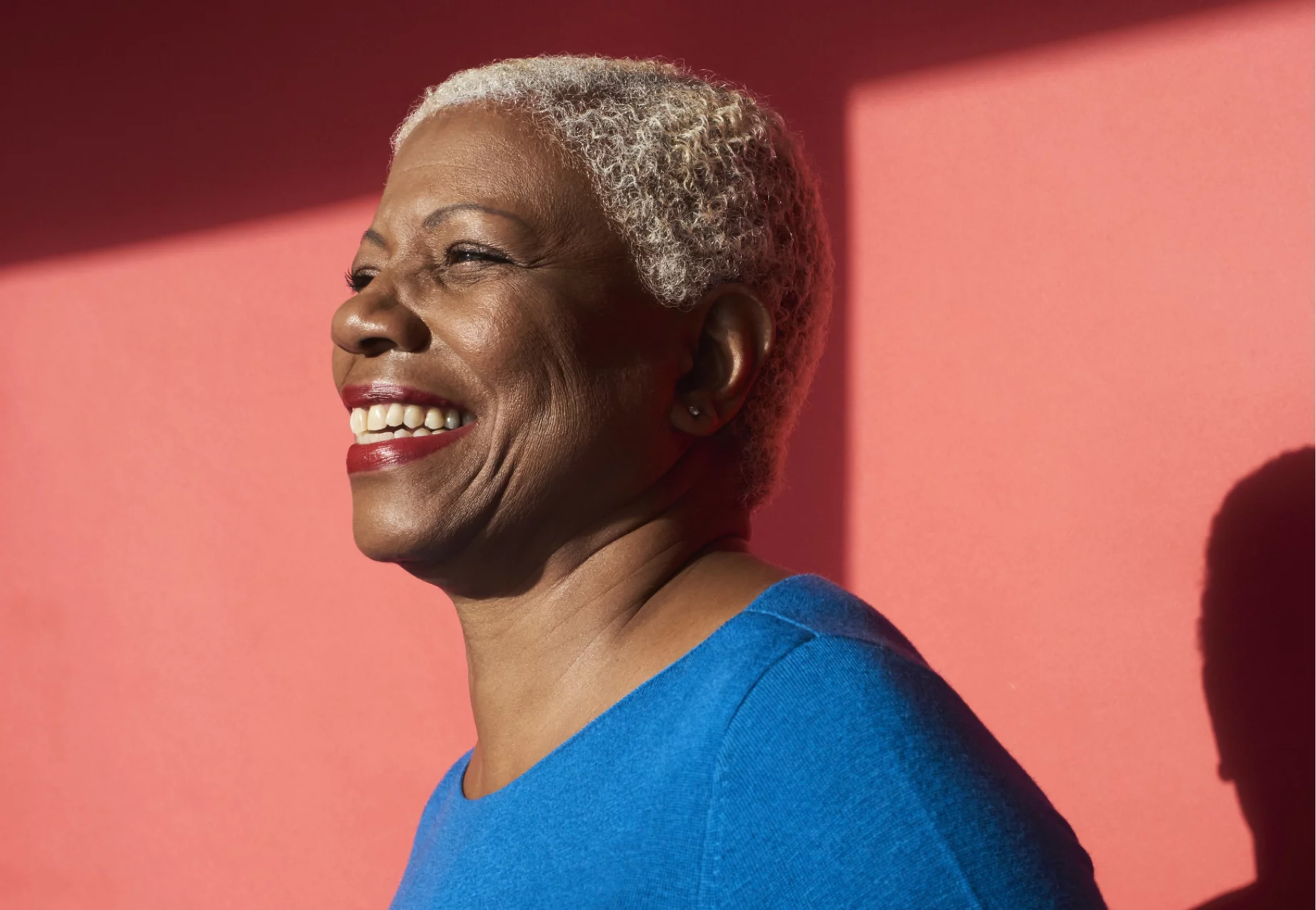 Smiling individual with a blue shirt and lipstick with a red background