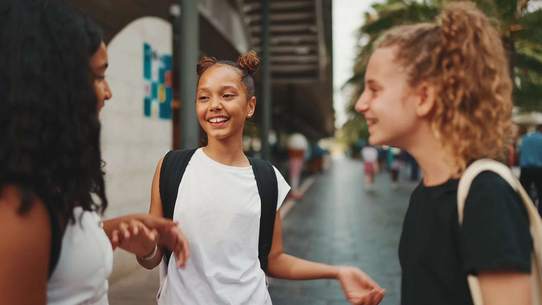 Three girls friends pre-teenage stand on the street smiling and emotionally talking, playing, clapping their hands. Three teenagers on the outdoors in urban cityscape background