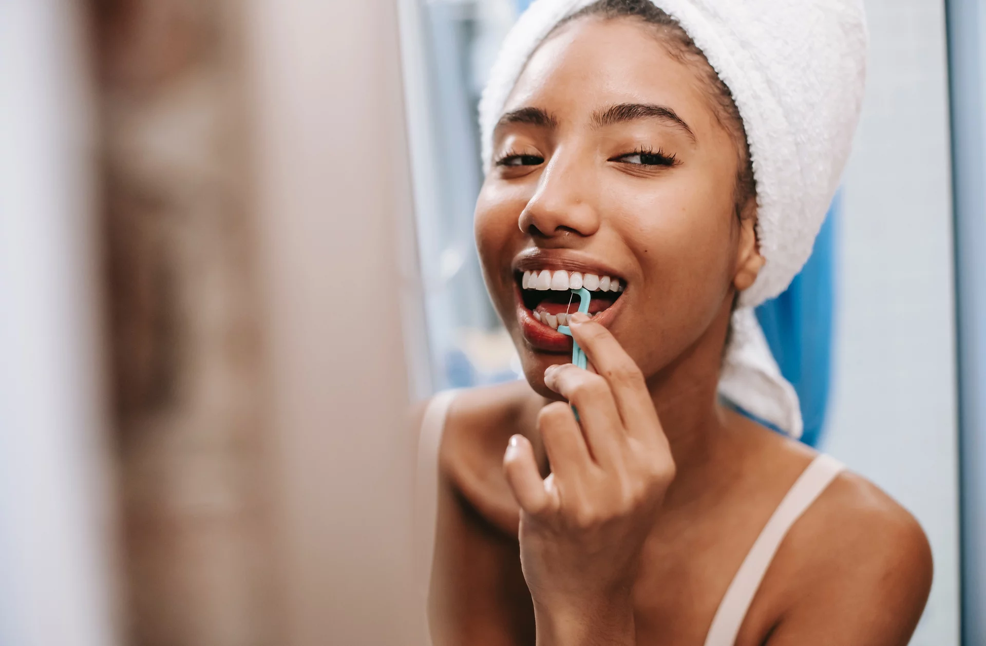 individual with beautiful teeth flossing in front of the mirror