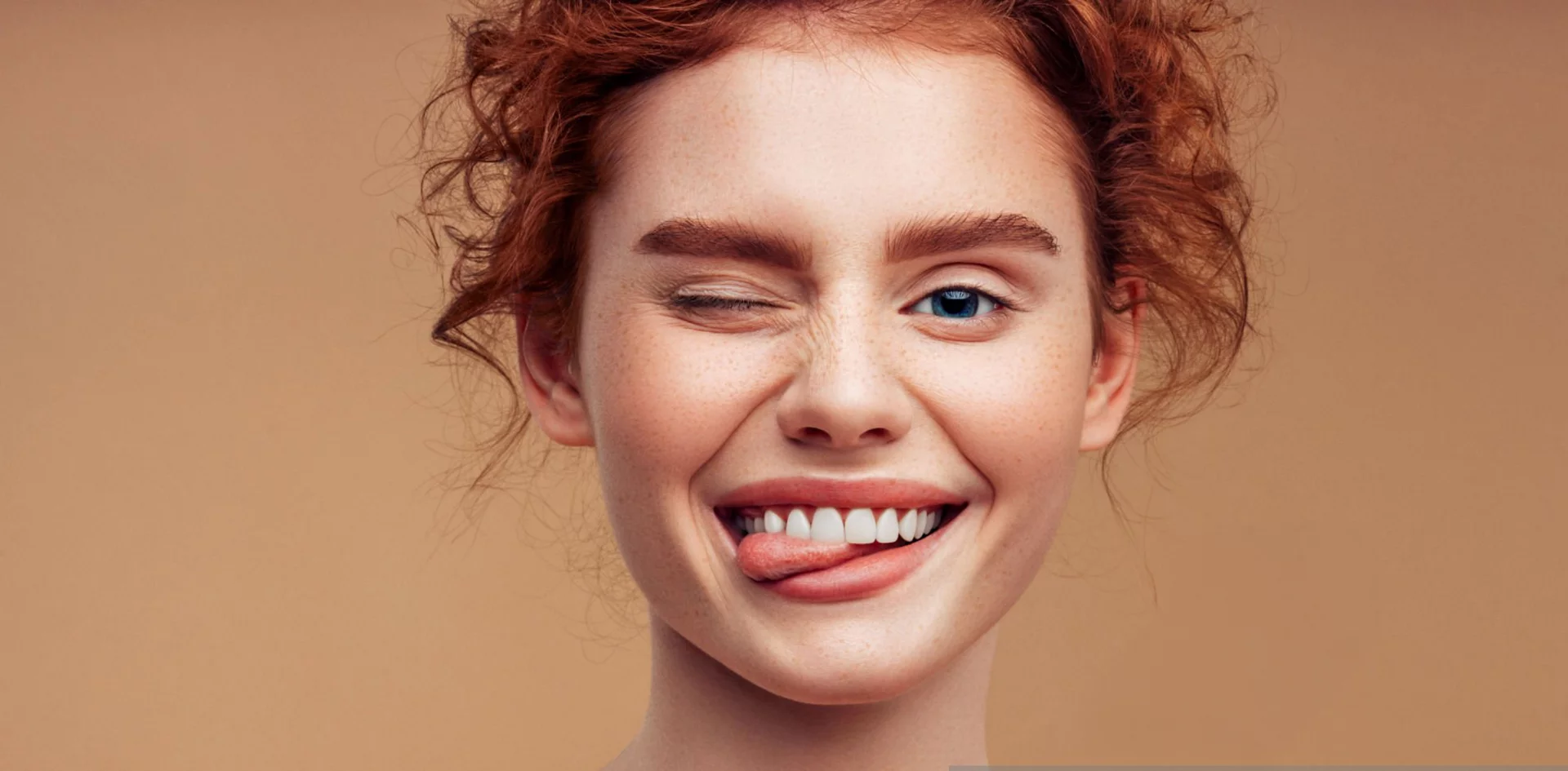 Individual with beautiful teeth smiling with their tongue out on a brown background