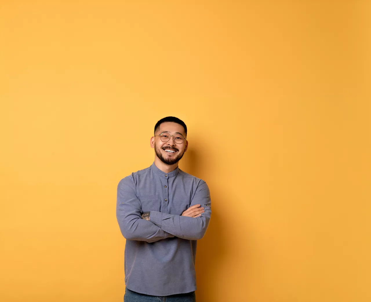 Confident young asian man standing with folded arms over yellow background