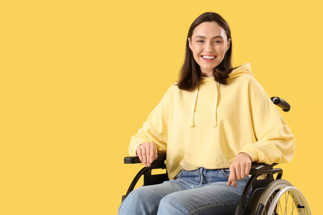 Happy young woman in wheelchair on yellow background