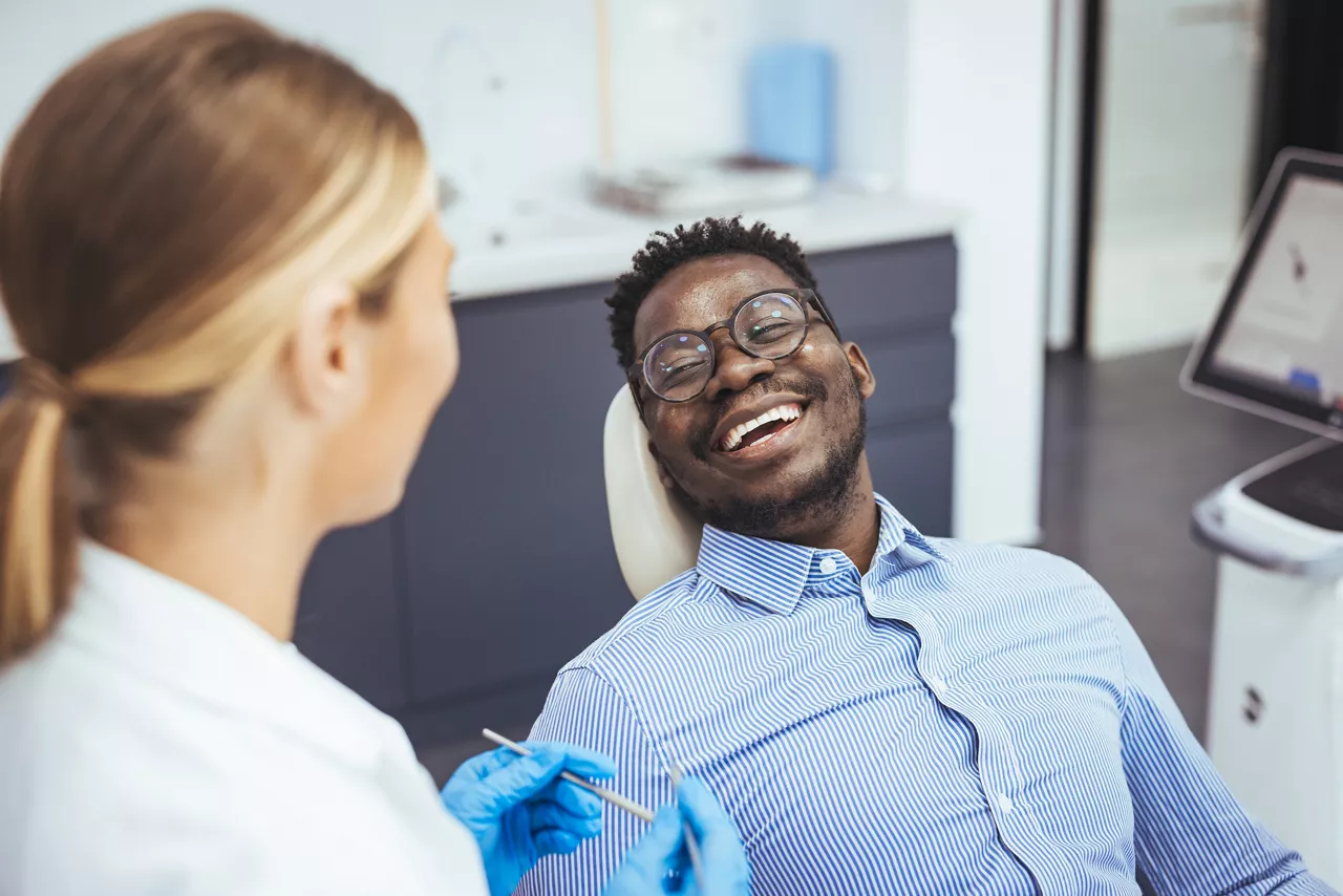 Smiling african guy in dentist chair looking with trust at his doctor, close up. Young African American Man Getting Teeth Treatment With Professional Stomatologist At Modern Clinic