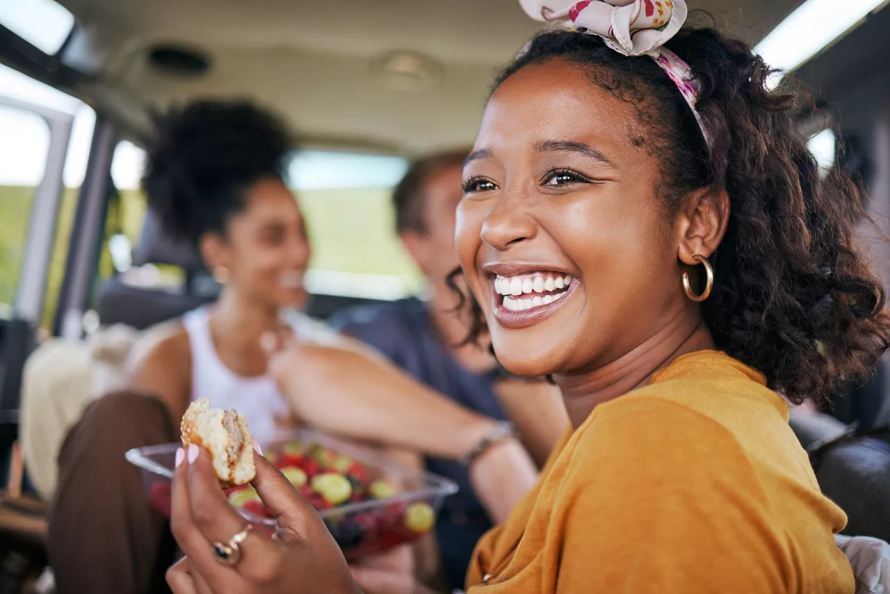 Happy black woman, smile and eating on road trip adventure with friends in travel for summer vacation or journey. African American female smiling and enjoying a healthy meal for holiday traveling.