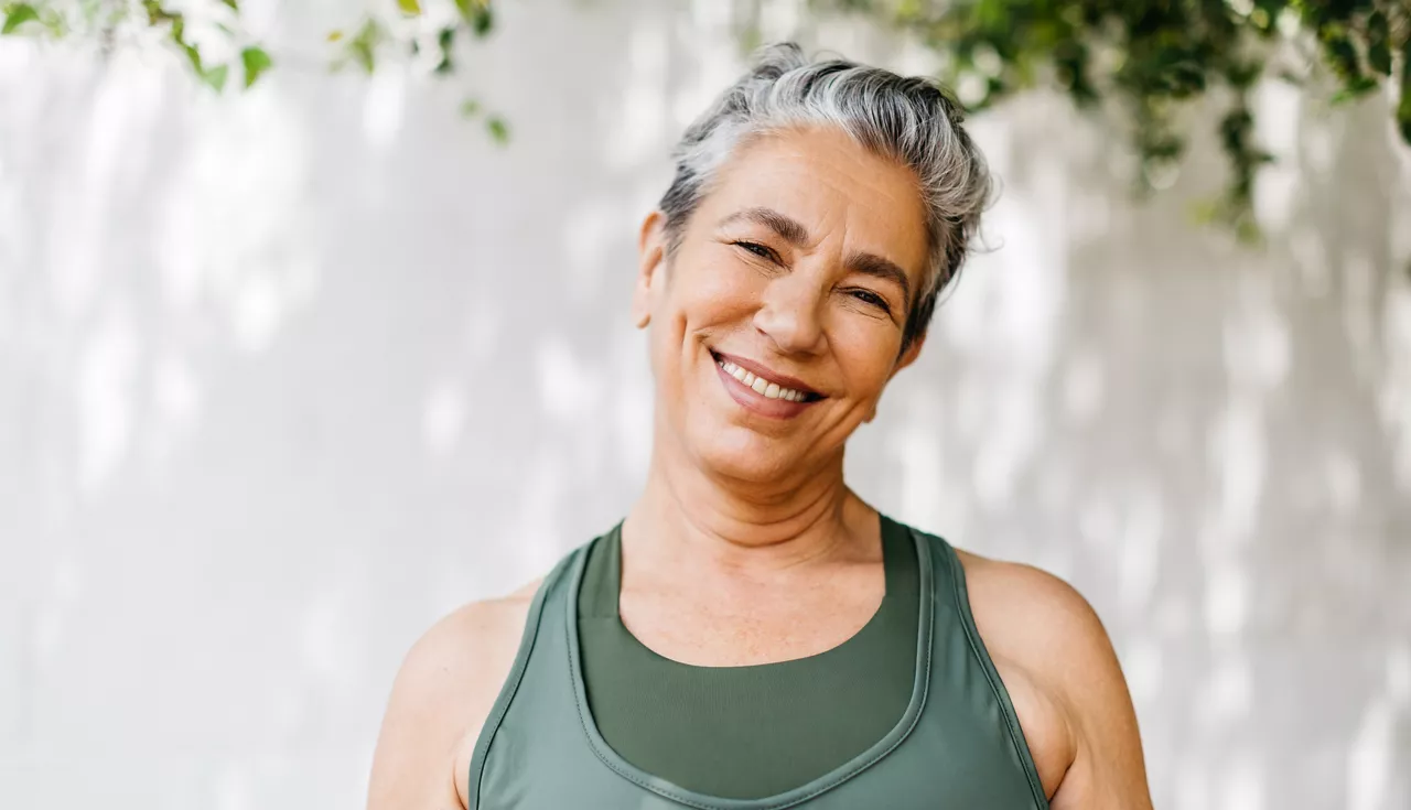 Mature woman looking at the camera with a happy smile as she takes on her outdoor workout routine in the morning. Retired woman taking an active approach to staying healthy, practicing regular exercise in her lifestyle.