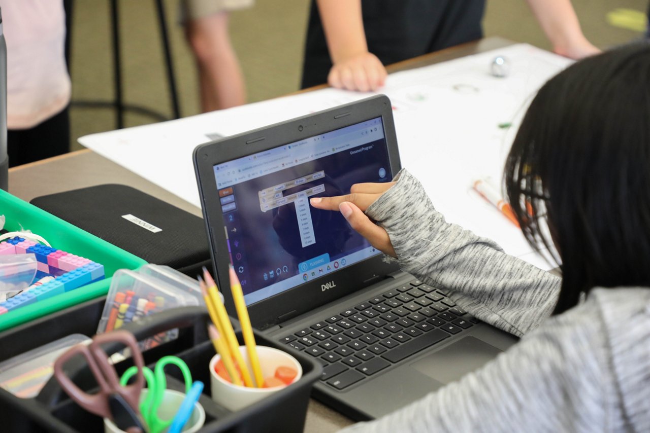 A person points at a laptop screen in a classroom