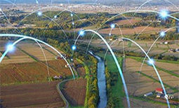 A rural landscape with farmland, farms, and a small city in the background, with bouncing points of light that represent data transfer
