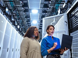 2 women look at a laptop computer in front of a bank of data center cabinets