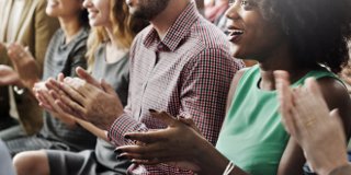 Group of men and women sitting in row smiling and clapping