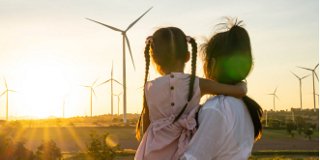 Back of woman holding child looking at wind turbines