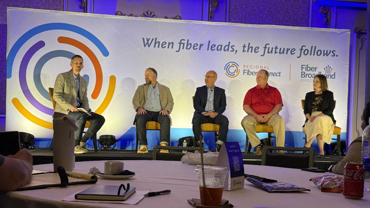 A panel of five people sitting on a stage at a fiber broadband association event