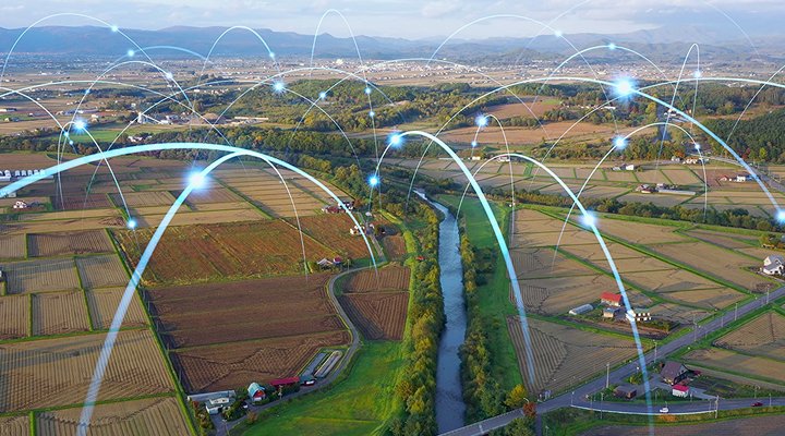 A rural landscape with farmland, farms, and a small city in the background, with bouncing points of light that represent data transfer