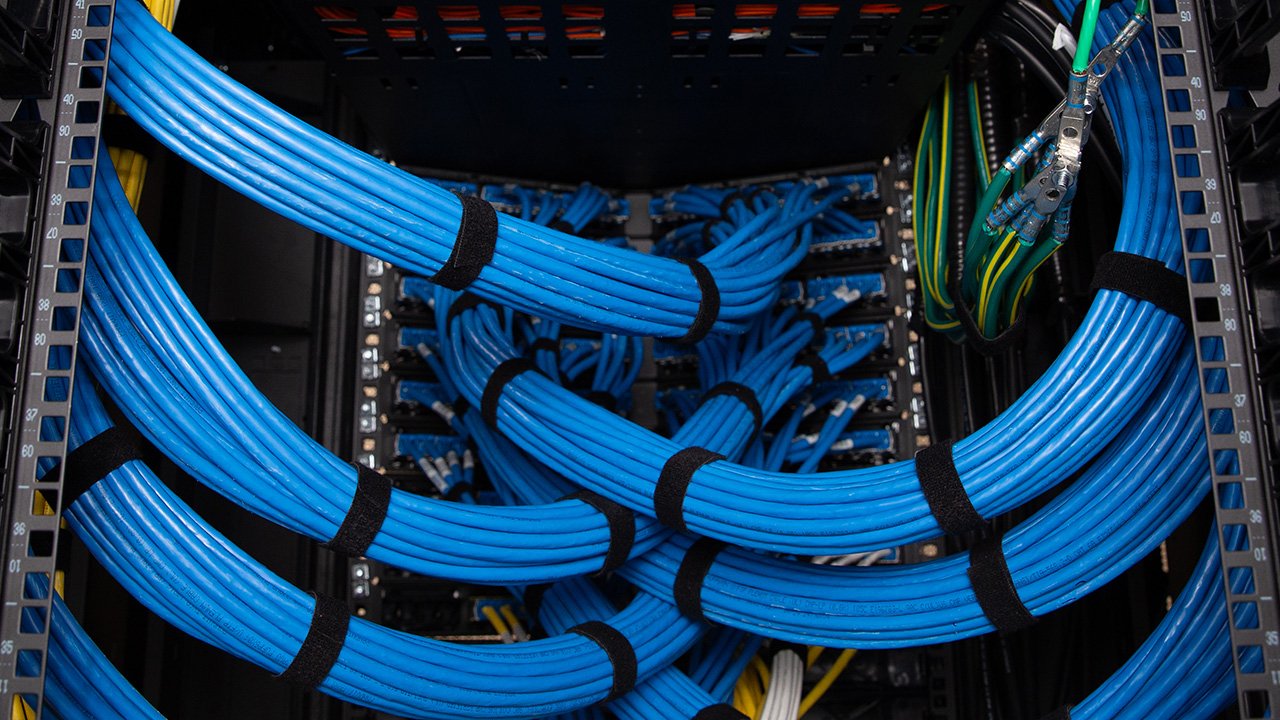 Bundles of blue copper cables routed into the back of a telecommunications rack