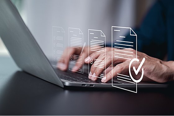 A person typing on a laptop computer, with an overlay image of pages with a checkmark showing compliance