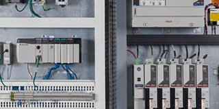 Industrial control panel with neatly organized wiring, programmable logic controllers, circuit breakers, and communication modules mounted on a metal backplate, with labeled terminals and structured cable management across multiple sections.