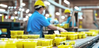 Products on a conveyor belt, with workers in hard hats blurred in the background