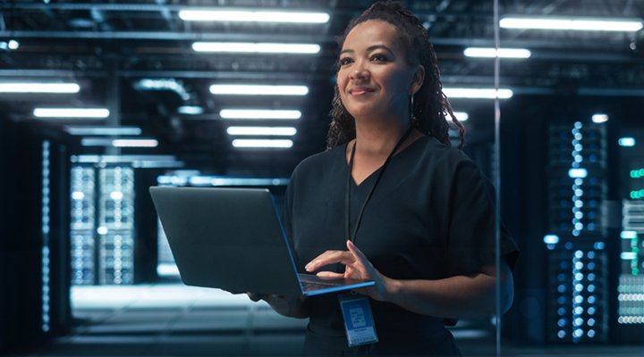 Data Center Operator working on a laptop inside a modern data center with rows of cabinets, server racks, and advanced network infrastructure in the background