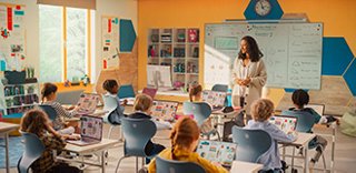 A teacher in a classroom, instructing young students who are using computers