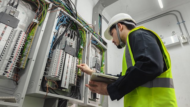 Electrical Engineer team working front control panel, An electrical engineer is installing and using a tablet to monitor the operation of an electrical control panel in a factory service room.