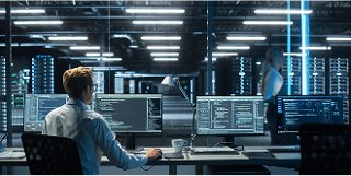 An image of an enterprise network with male at desk looking a computer screen facing data center