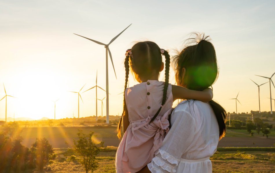Back of woman holding child looking at wind turbines
