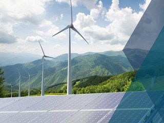 Solar panels and wind turbines stand in a mountainous landscape, showcasing renewable energy in a natural setting.