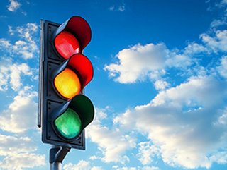 A traffic signal with red, yellow, and green lights against a blue, cloudy sky