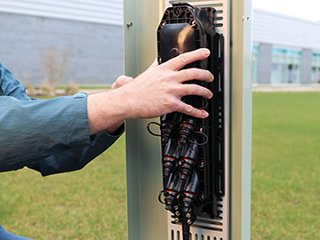 a person installing a multiport service terminal in a broadband pedestal surrounded by green grass with a building in the background
