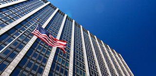 high-rise building against a blue sky, with a US flag in front of the building