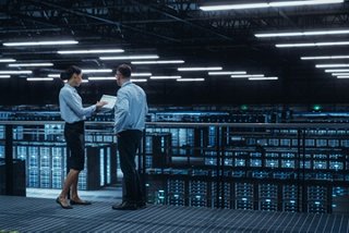 Two IT professionals reviewing cloud infrastructure plans on a tablet inside a hyperscale data center