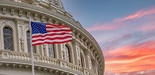 closeup of a government building with a US flag, against a colorful sky