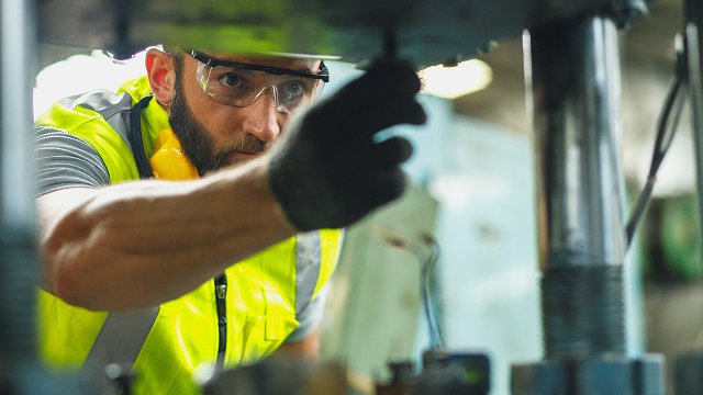 Close up of male engineer looking of working at industrial machinery setup in factory.