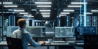 Data Center manager working at a multi monitor workstation inside a modern data center reviewing thermal temperatures