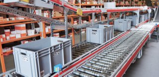 A view of a shipping and packaging facility, showing a conveyor belt with white baskets on top of the belt. 