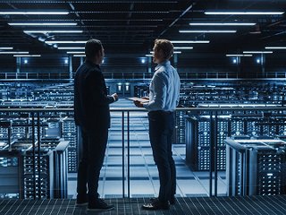 Men looking at rows of data cabinets in server room from a balcony