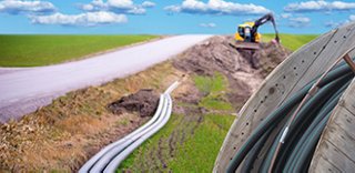 Heavy equipment is faded in the background, digging a trench to lay fiber optic cable for rural broadband deployment