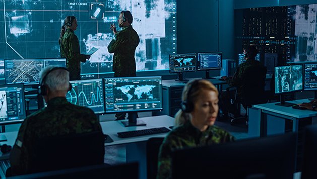 Military personnel work in a secure room filled with monitors and screens
