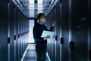 Technicians inspecting server cabinets in a secure on-premises edge data center while holding a laptop for real-time monitoring