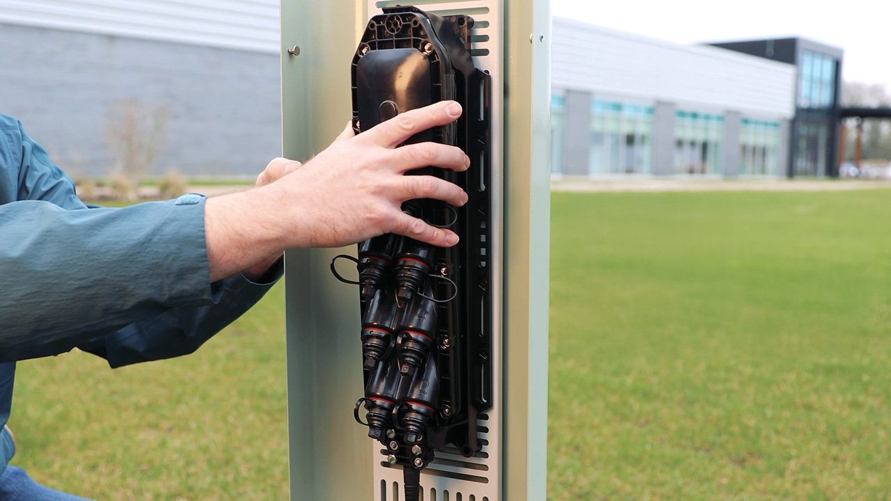 An open metal pedestal with a technician installing a multiport service terminal, positioned in a yard in front of a building