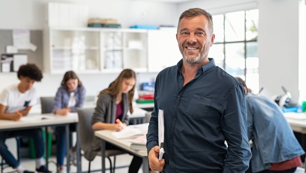 A teacher in a classroom, with students working at desks in the background
