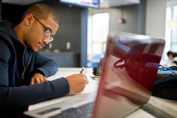 a male student studies with a laptop open beside him