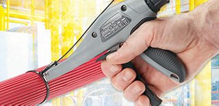 Hand holding a cable tie installation tool, with a cable tie wrapped around a bundle of communications cabling