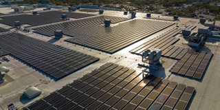 Aerial view of blue photovoltaic solar panels mounted on industrial building roof 