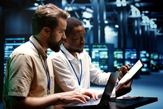 Two IT specialists collaborating on cloud and network solutions using a laptop and tablet in a modern data center environment
